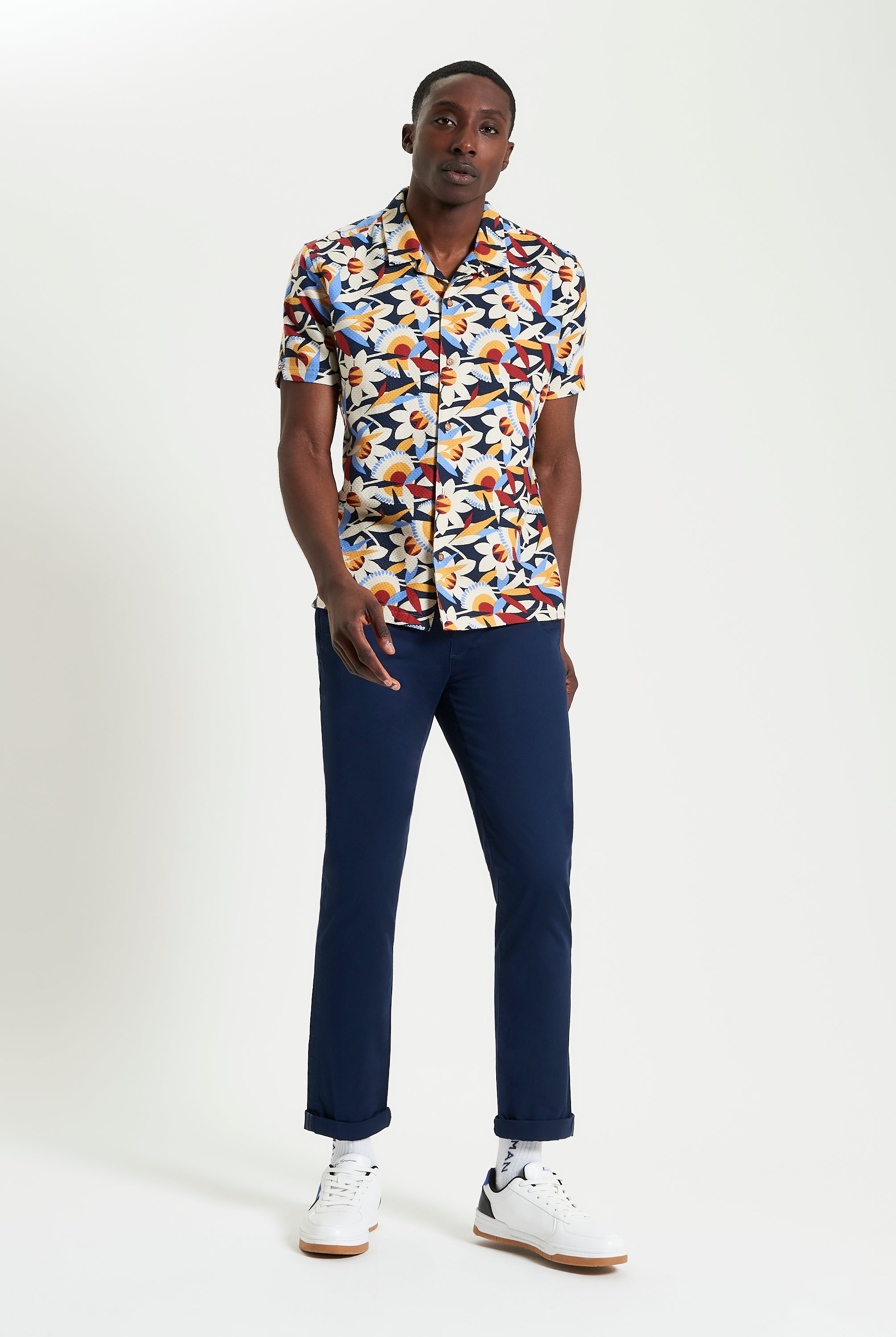 Abstract Floral Print – Bold pattern short-sleeve shirt model wearing navy trousers and white sneakers.