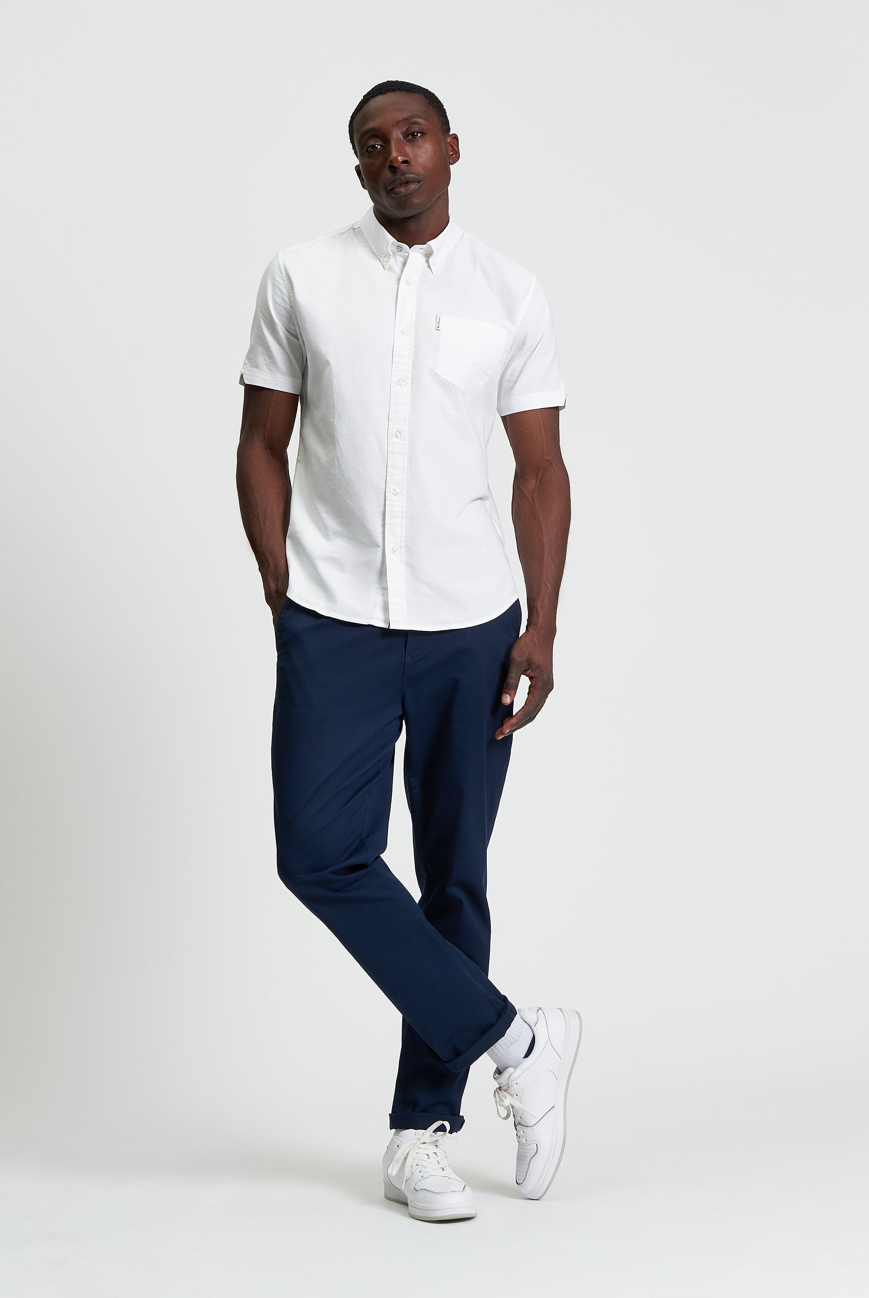 Model wearing a White Signature Oxford Short Sleeve Shirt with black pants and white sneakers, showcasing a modern style.
