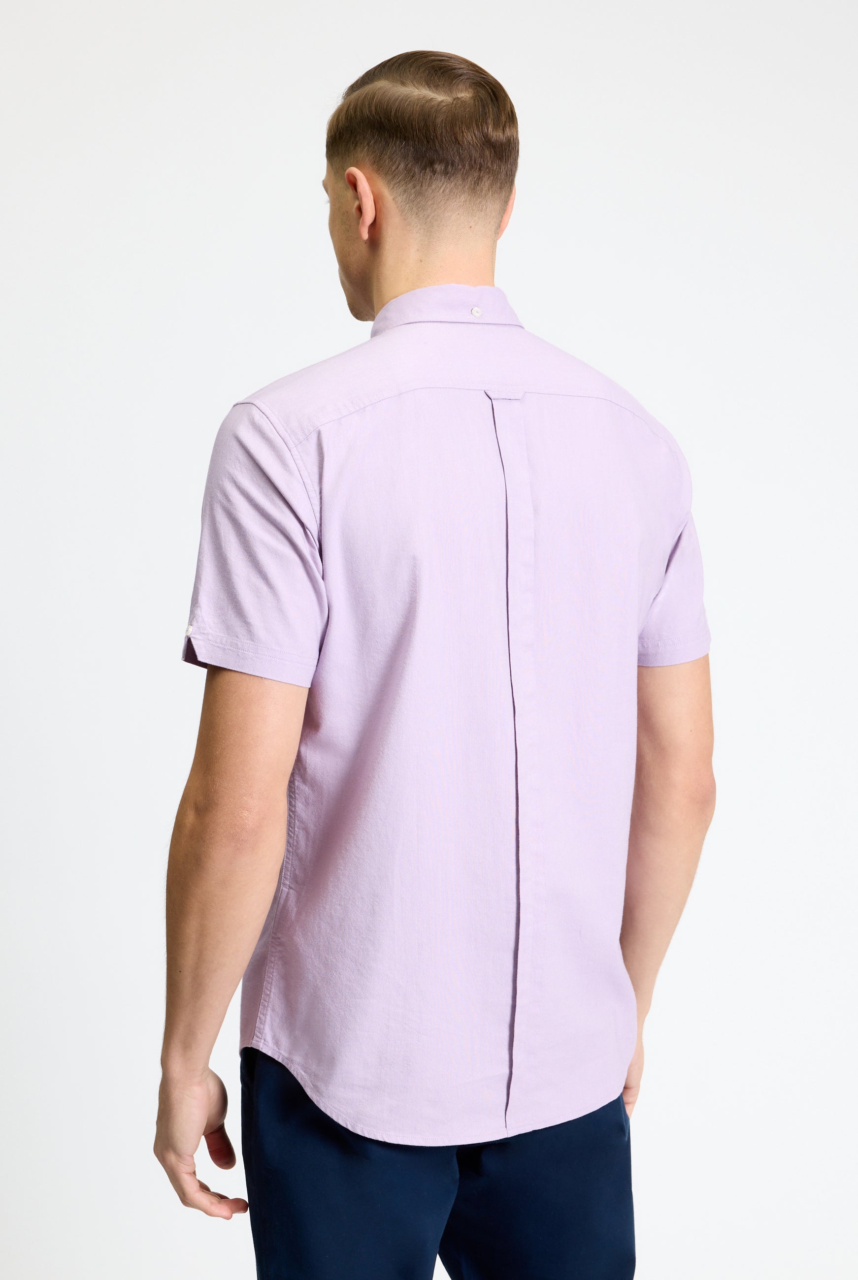 Back view of a man wearing the Signature Oxford Short Sleeve Shirt in light purple, featuring a button-down collar and back pleat.