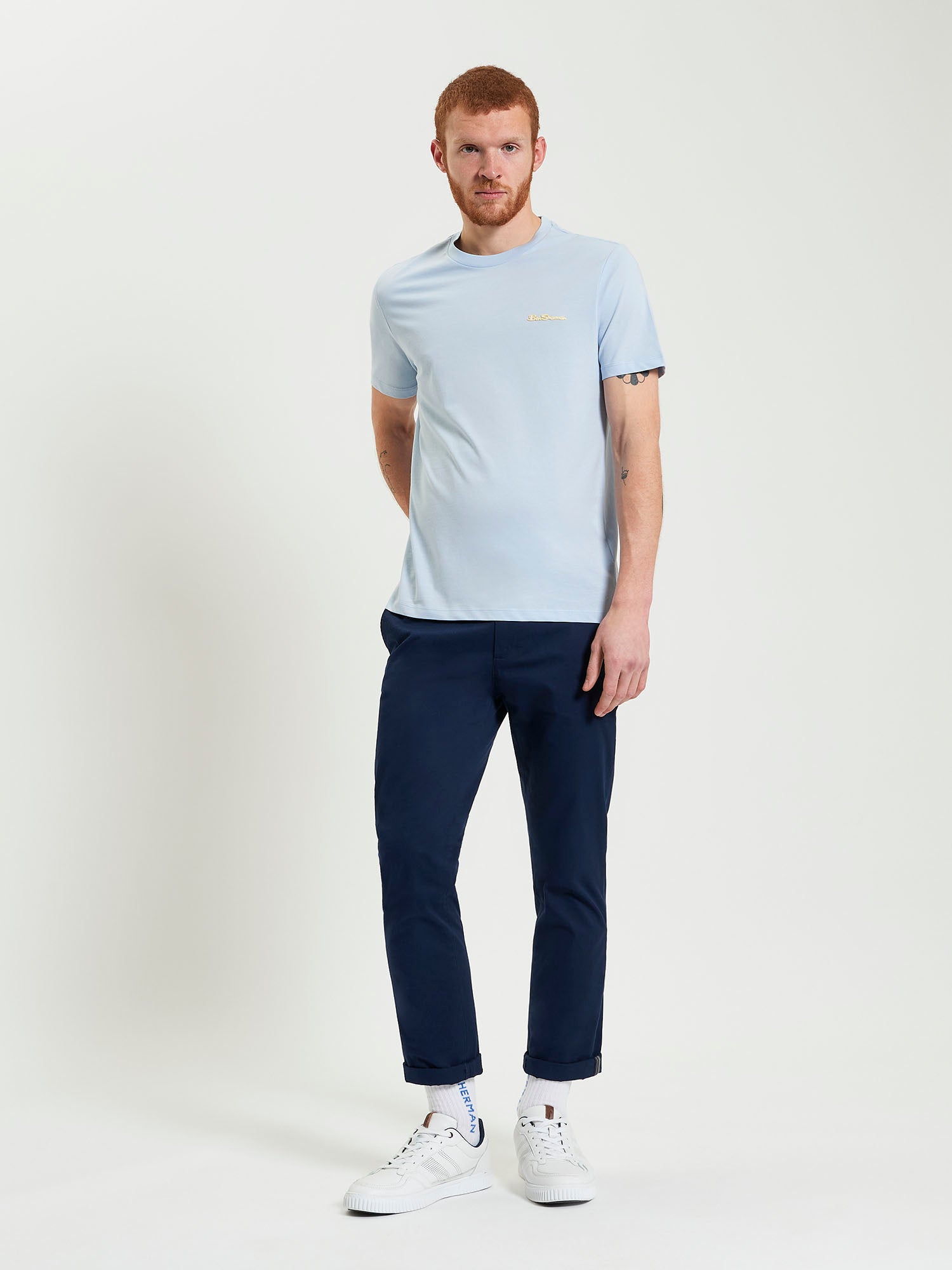 Signature Tee – light blue crew neck with branded silicon badge, styled with navy pants, ideal for casual wear.