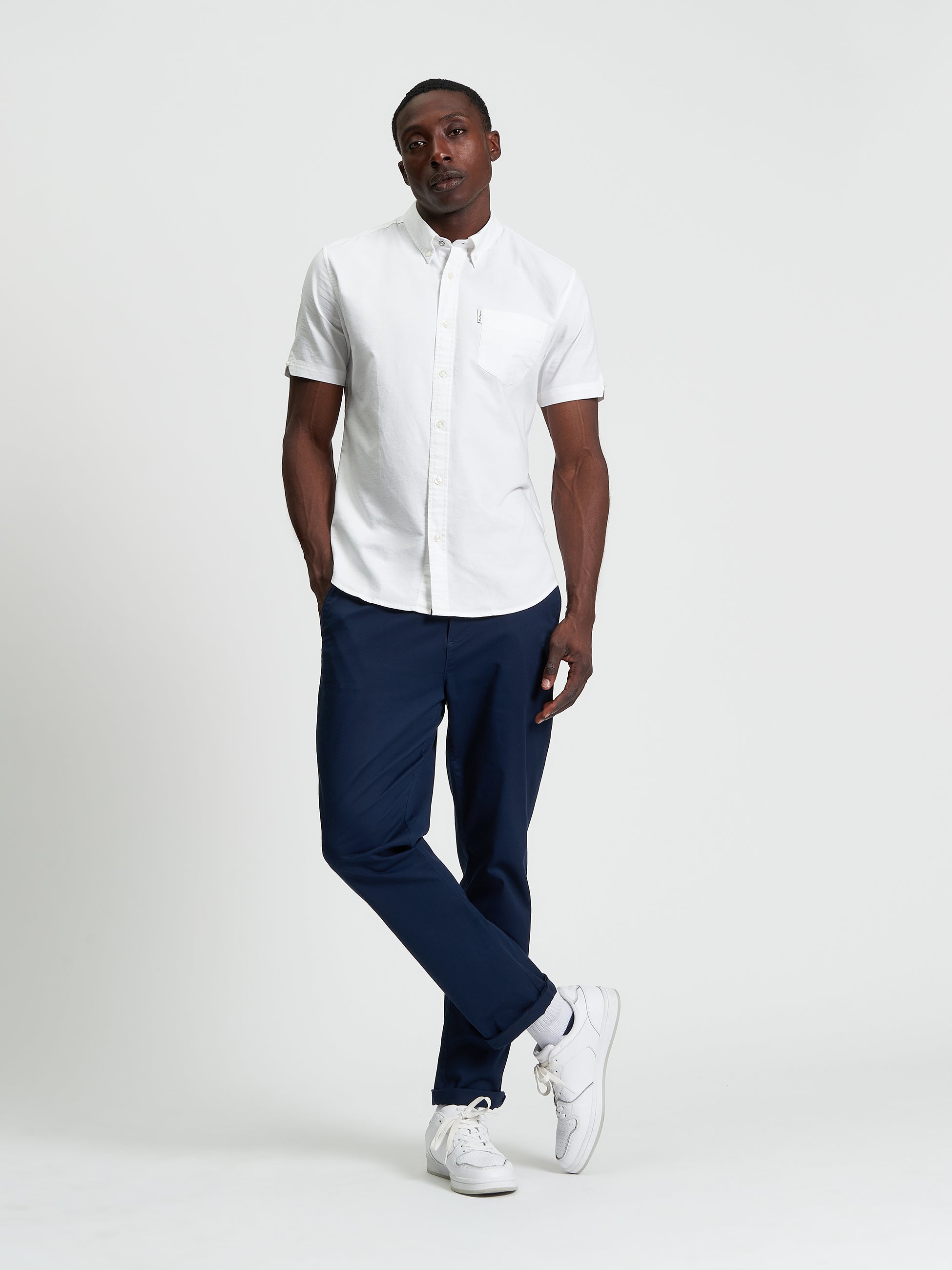 Model wearing a White Signature Oxford Short Sleeve Shirt with black pants and white sneakers, showcasing a modern style.