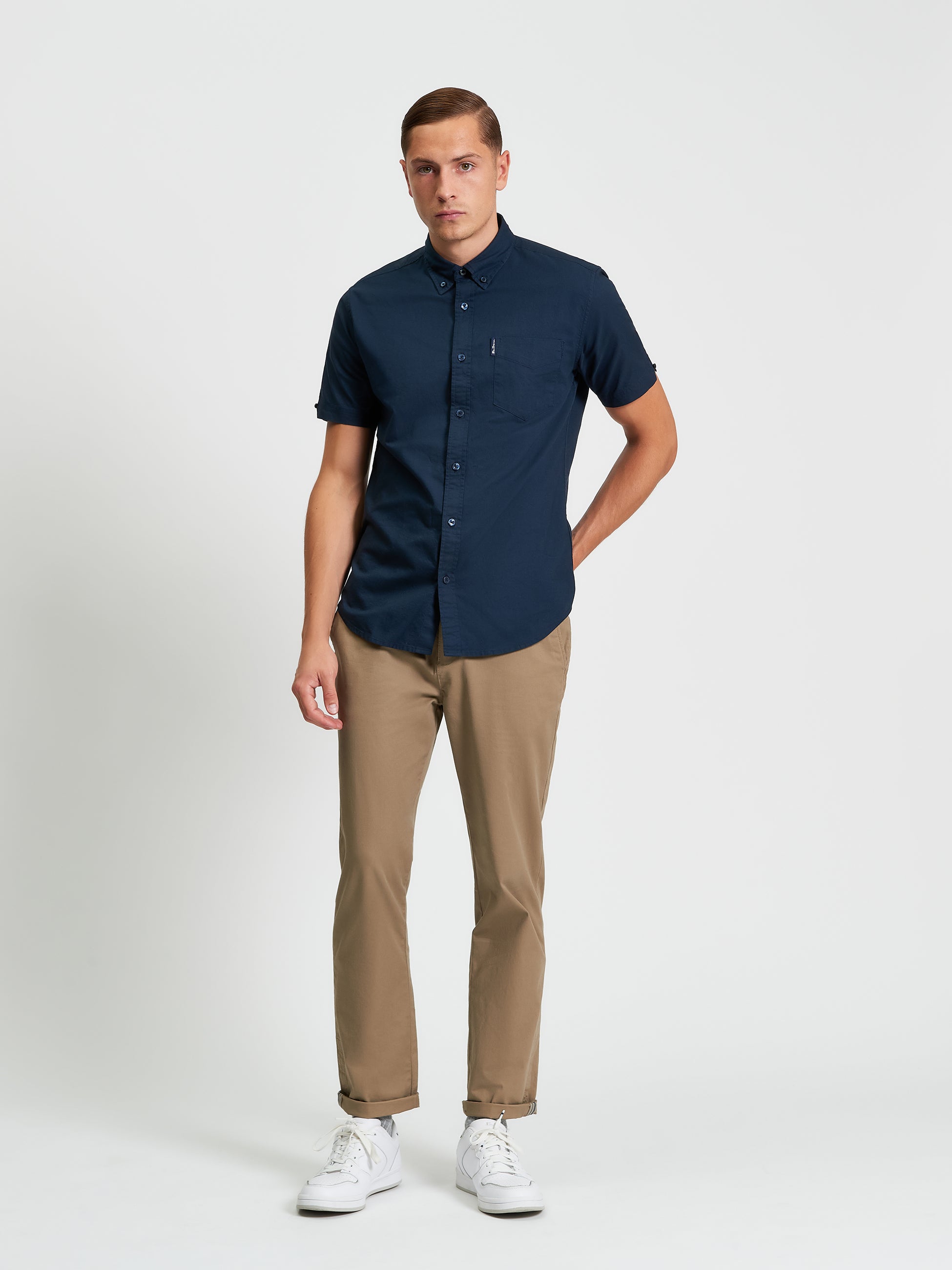 Model wearing a Navy] Signature Oxford Short Sleeve Shirt with black pants and white sneakers, showcasing a modern style.