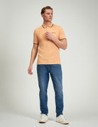 Signature Pique Polo – stylish man wearing a peach-colored polo shirt with contrast detailing and jeans.