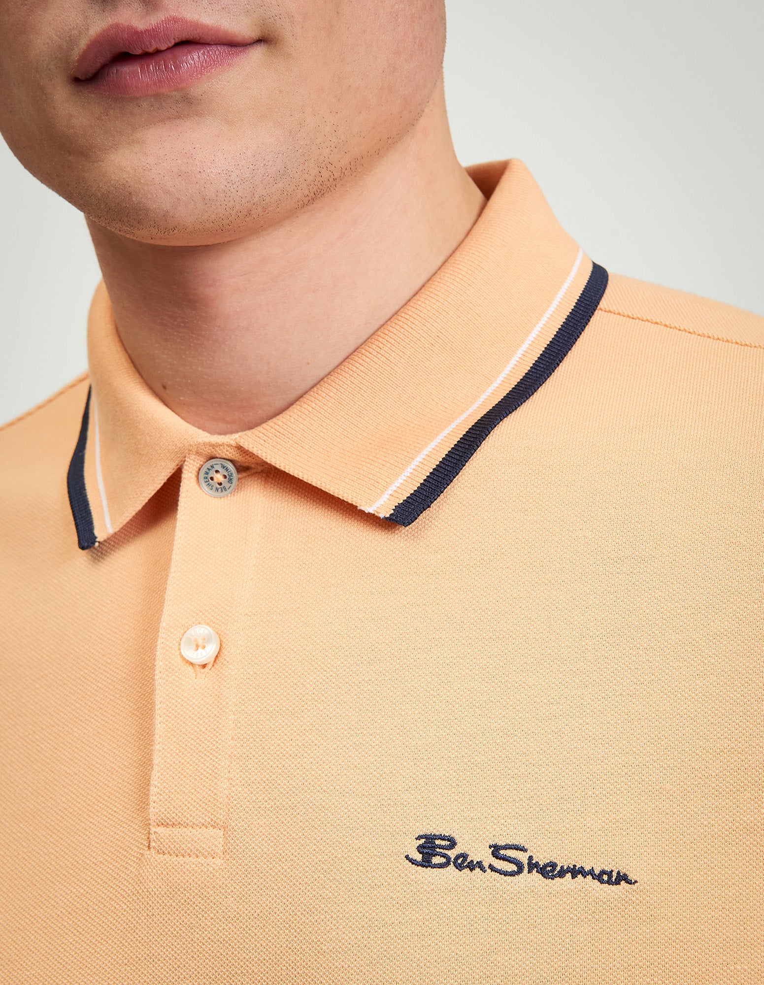 Close-up of Signature Pique Polo in peach with contrast collar, featuring Ben Sherman logo embroidery.