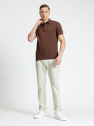 A model showcasing the Signature Short Sleeve Polo in brown, paired with light pants and white sneakers.