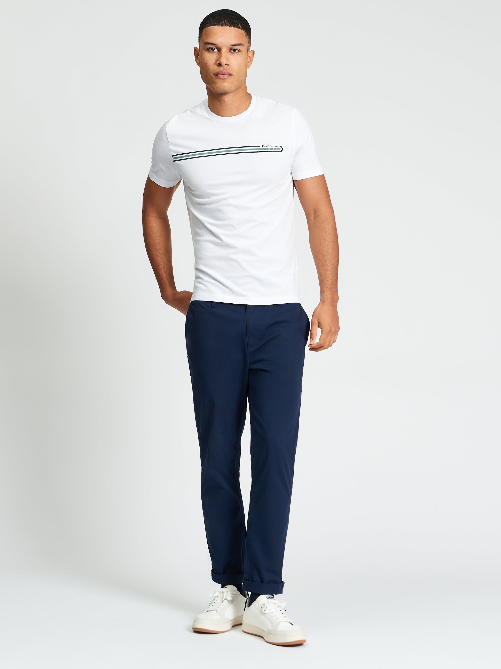 Core Stripe Tee – White men's t-shirt with printed chest stripes, paired with navy pants and white sneakers.