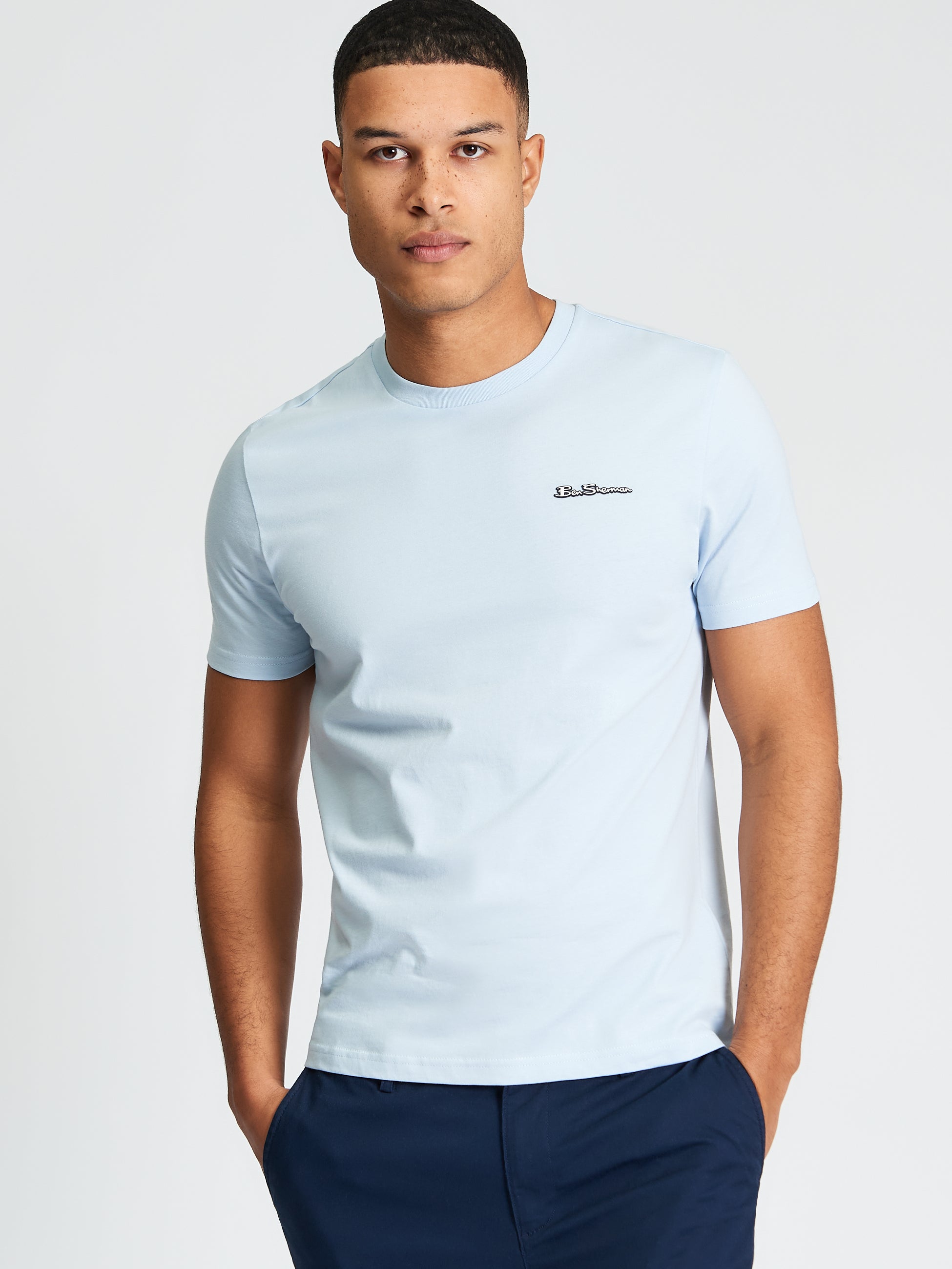 Signature Tee – light blue crew neck shirt on model with branded badge, perfect for casual wear.