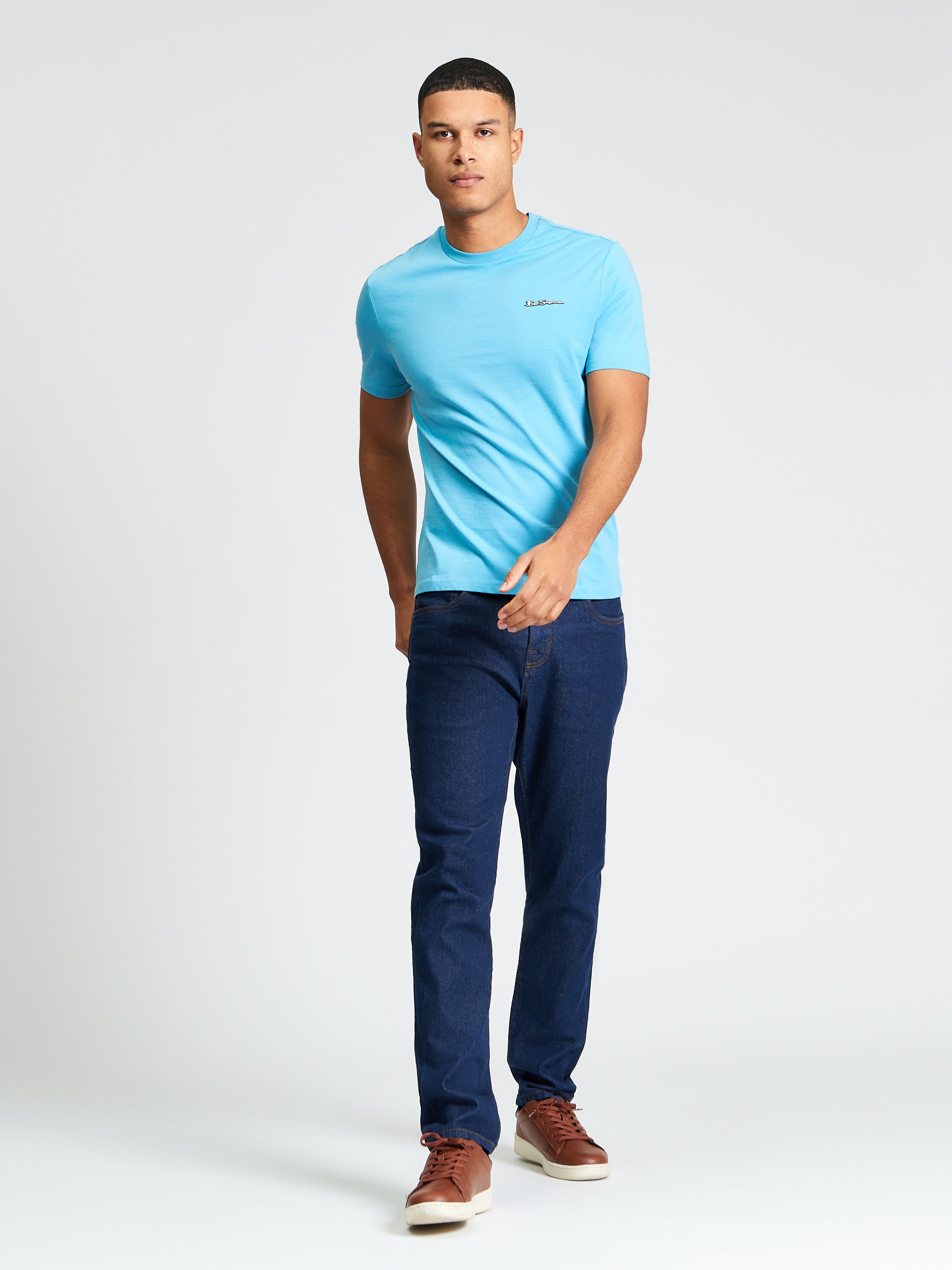 Signature Tee – Light blue crew neck t-shirt worn by a man with dark jeans and brown sneakers.